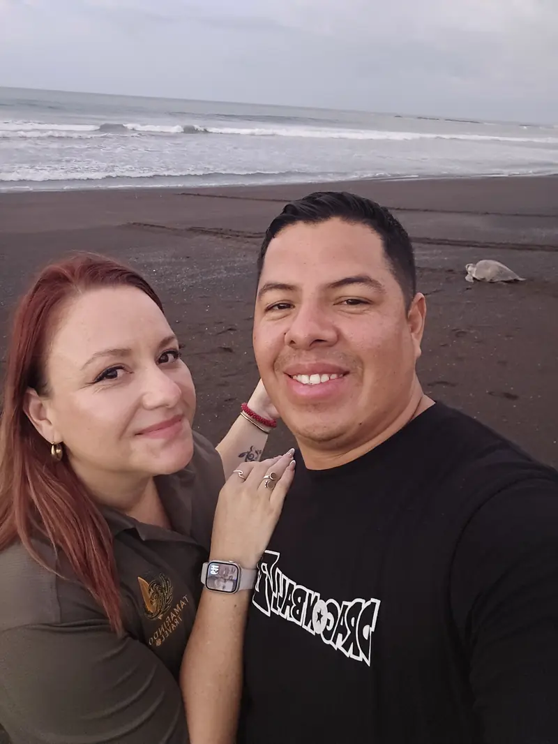 Cindy Porras and Dennis Apu, founders of Tamarindo Travel, on the beach at sunset with a sea turtle behind them