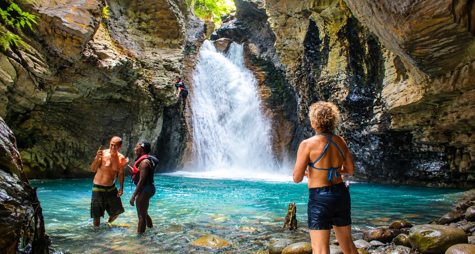 Guests standing in a turquoise pool below La Leona waterfall inside a rock canyon near Liberia, Guanacaste